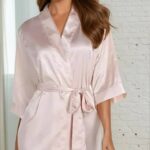 Kvinna i rosa morgonrock framför tegelvägg.